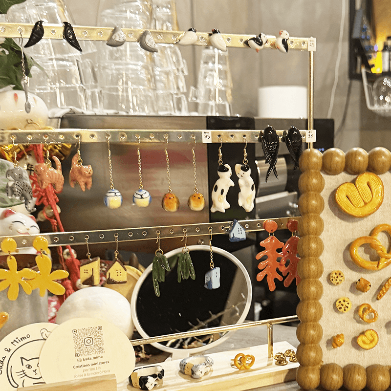 Miniature earrings and charms displayed on a brass rack at Camping X, Paris