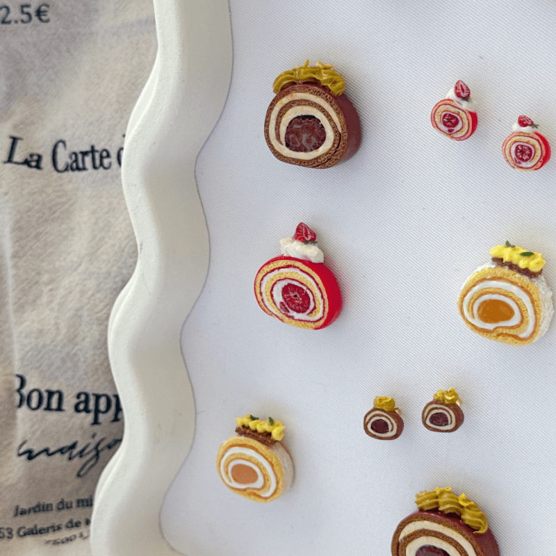 Miniature dessert-roll earrings displayed on a bakery-inspired tray